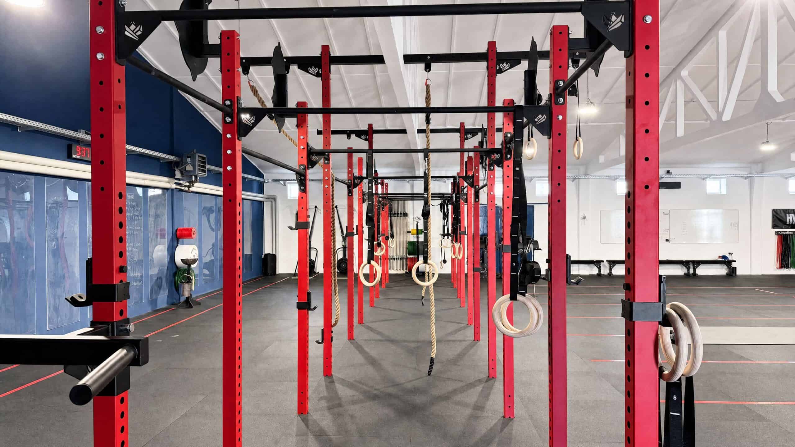 Modernes Krafttraining mit roten Racks und Turnringen im Fitnessstudio.
