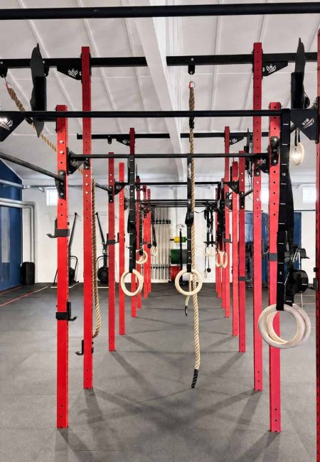 Modernes Krafttraining mit roten Racks und Turnringen im Fitnessstudio.